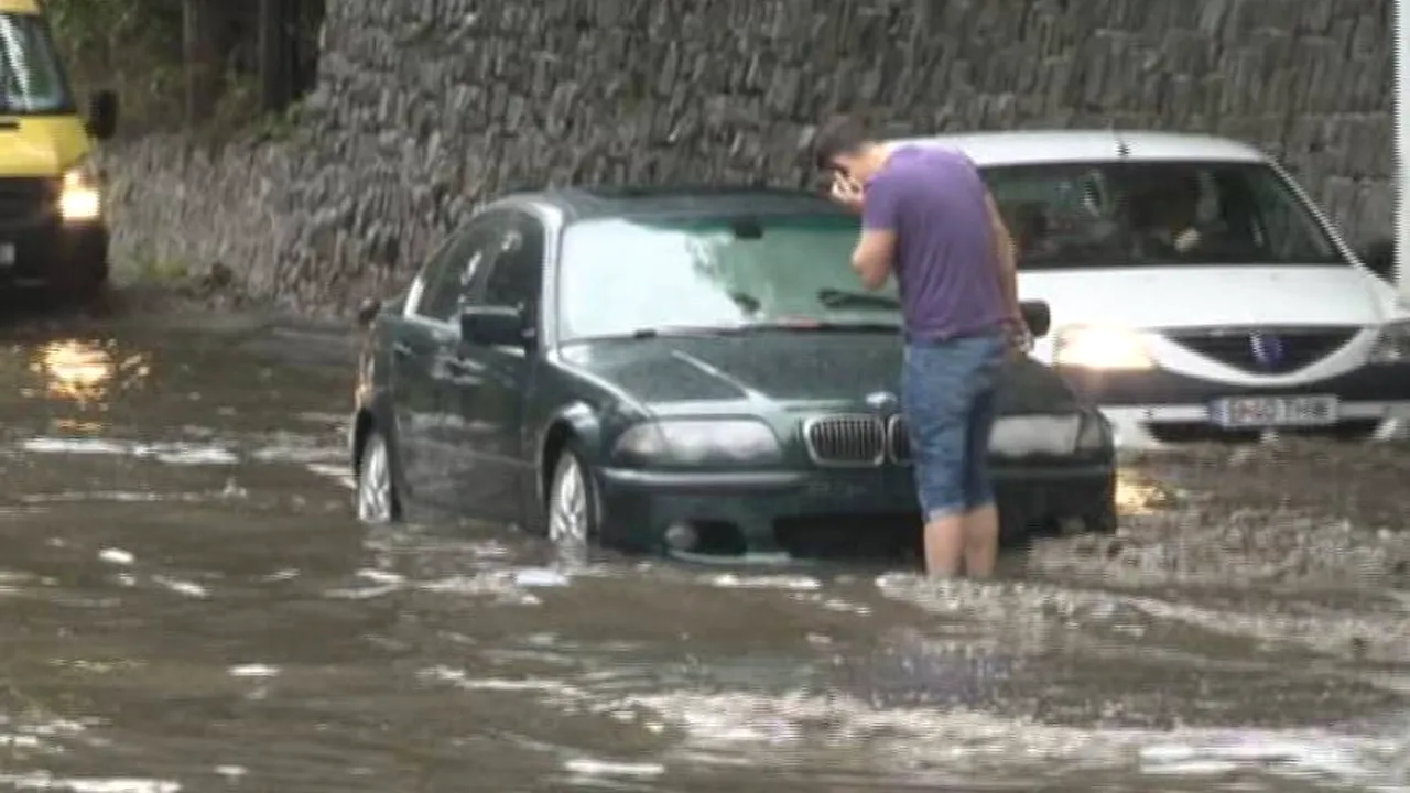 Apă de 15 cm, acumulată pe un drum naţional, după o ploaie torenţială. Circulaţia rutieră se desfăşoară cu dificultate 