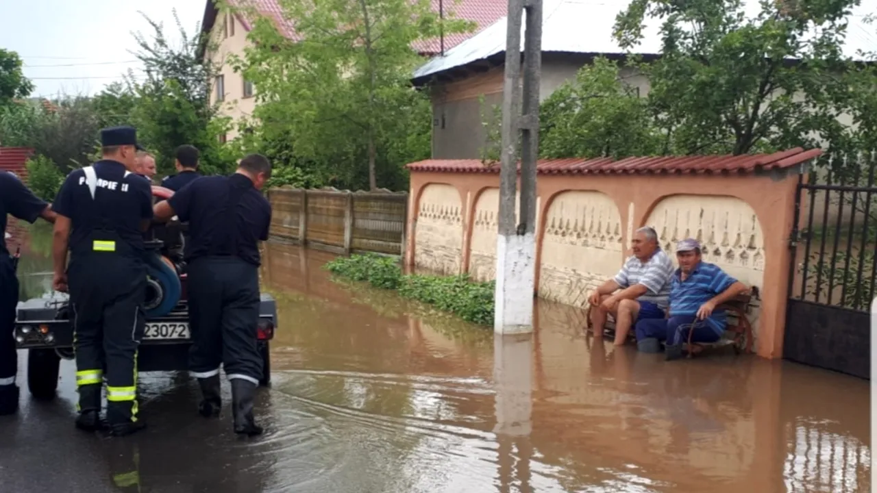 Fotografia zilei vine din Teleorman. Doi localnici stau pe bancă în timp ce pompierii scot apa din comună